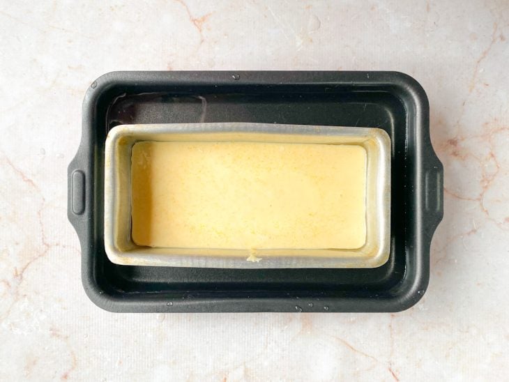 Massa de pão em uma forma untada que está dentro de outra forma maior com água.