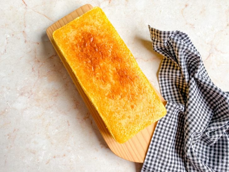 Pão de fubá desenformado sobre uma tábua de madeira pronto para consumo.