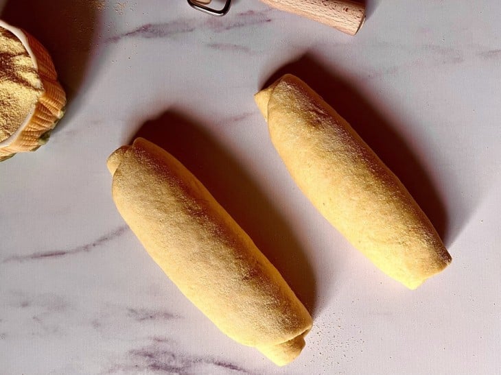 As duas massa de pão enroladas em formato de rocambole dispostas em cima de uma bancada.