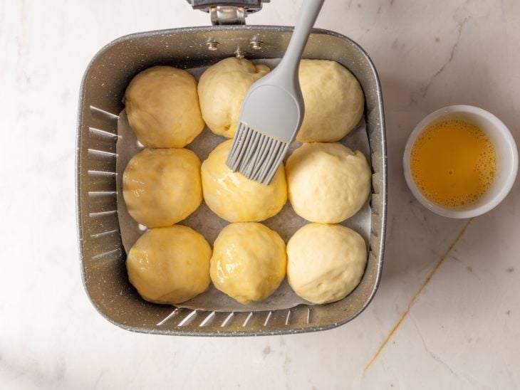 Mistura de gema com leite sendo pincelada sobre os pãezinhos.
