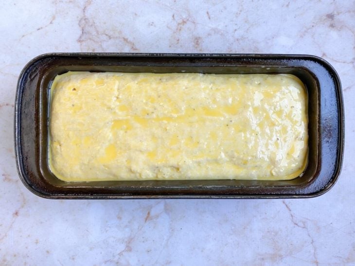 Uma forma com a massa do pão pincelada com leite e gema de ovo.