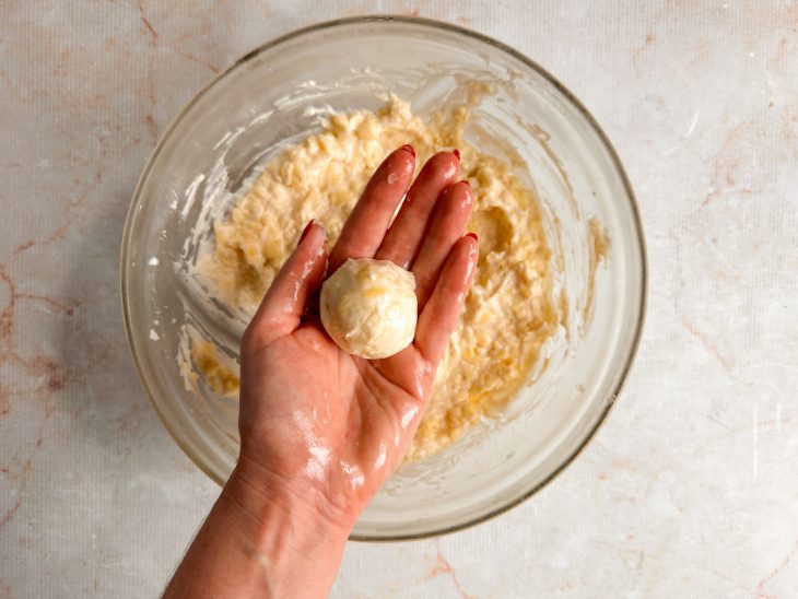 Porção de massa modelada em bolinha sobre uma mão untada.