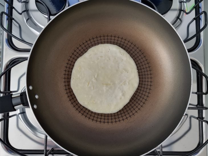 Frigideira com massa de pão de queijo em formato de disco.