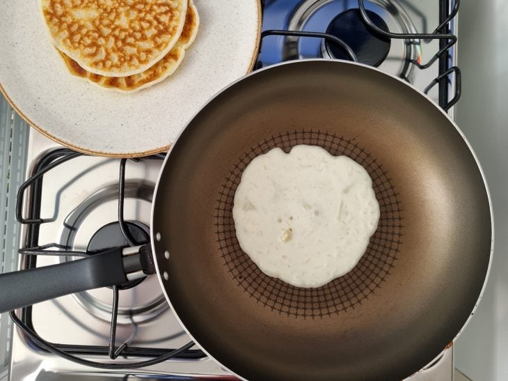 Panela com massa assando e prato ao lado com pães de queijos já assados.