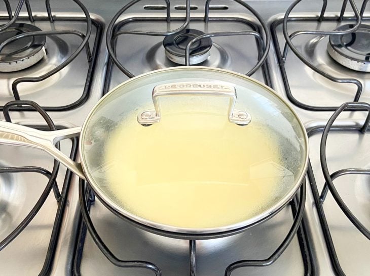 Uma frigideira com a massa de pão de queijo tampada ao fogo.