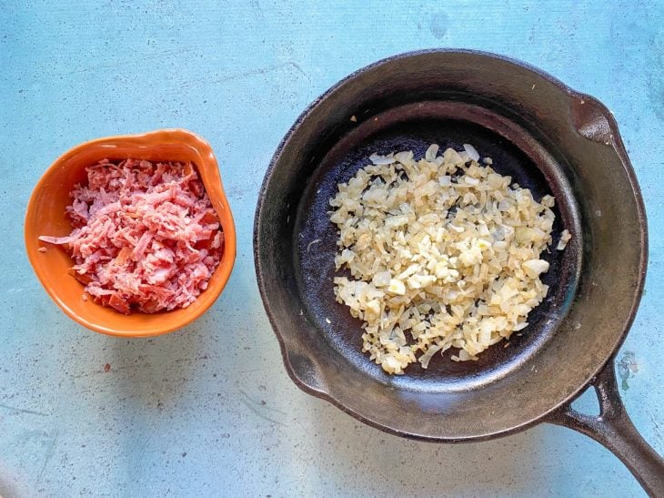 Uma frigideira contendo alho e cebola refogados e um recipiente contendo calabresa picada.