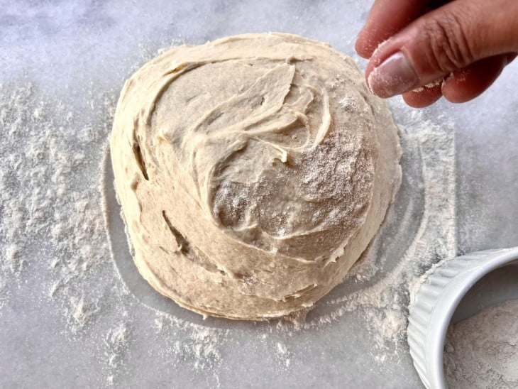 Uma mão polvilhando farinha de arroz na massa de pão crua.