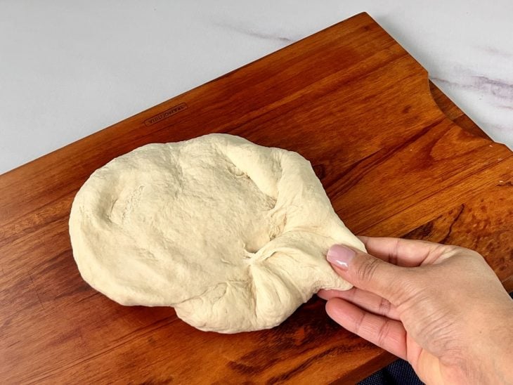 Uma tábua contendo a massa do pão sovada e lisinha.