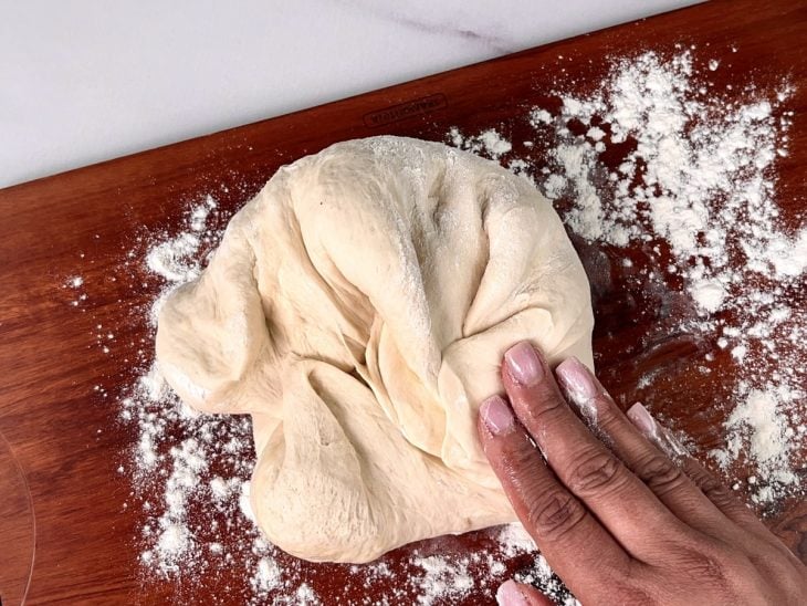 Uma tábua enfarinhada contendo a massa do pão sendo sovada.