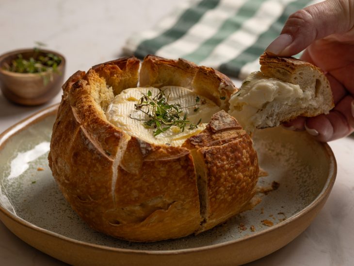 Pão e o queijo servidos. Uma fatia sendo tirada.