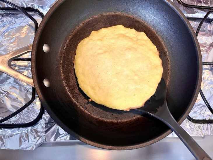 Pão low carb de frigideira com espátula em baixo da massa para virar.