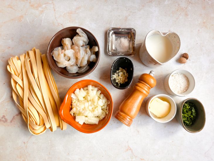 Ingredientes organizados sobre a bancada com alho amassado, cebola picada e camarões separados.
