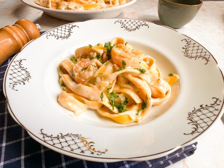 Massa finalizada com salsinha e camarões decorando o prato.