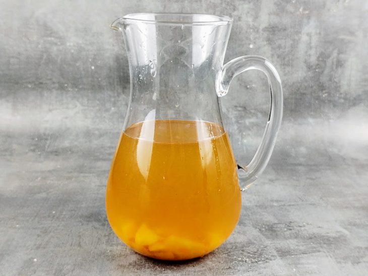 Pêssegos picados, calda da fruta, suco dos limões e açúcar adicionados a jarra com chá.