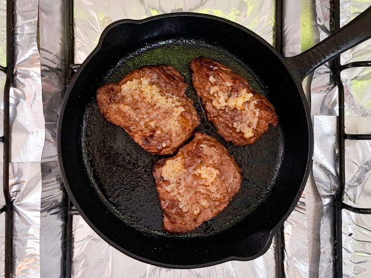 Numa frigideira, a carne quase pronta, com uma camada da pasta de alho por cima.