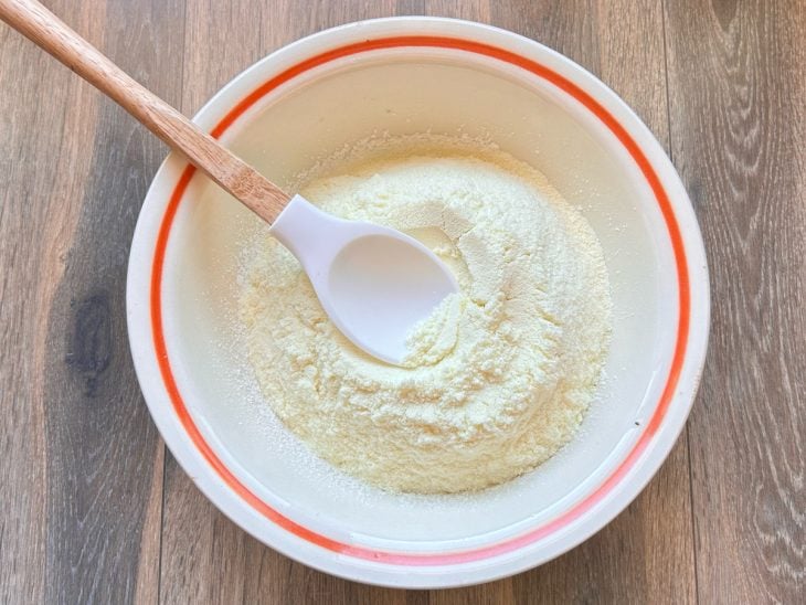 Uma colher e uma tigela com a mistura de leite em pó e açúcar de confeiteiro.