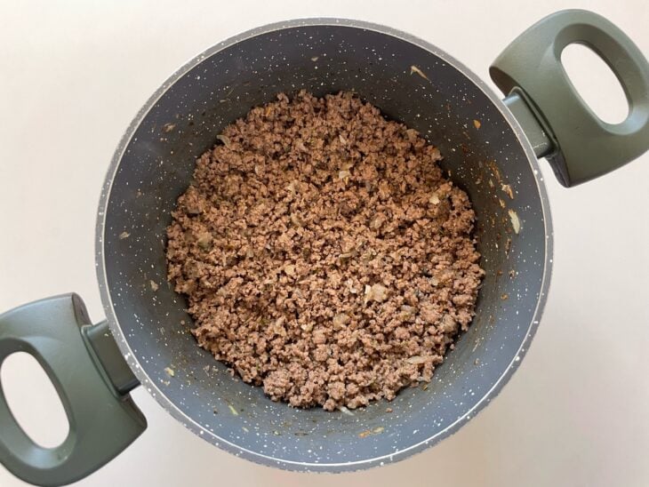 Cebola e alho sendo adicionados à carne e refogados até ficarem macios e aromáticos.