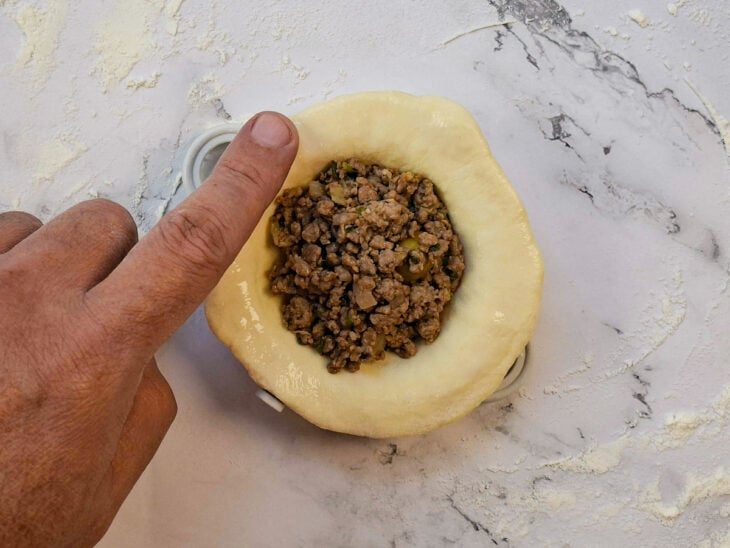 Disco de massa aberto com rolo e recheado com carne moída já fria.