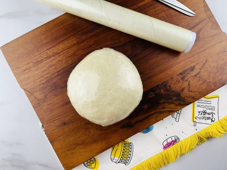 Uma tábua com massa de pastel coberta por plástico-filme.