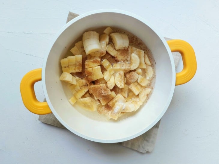 Banana, canela, açúcar e outros ingredientes do recheio em uma panela branca.