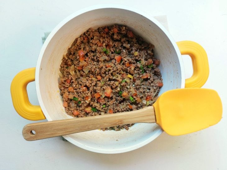 Carne moída com alguns temperos coloridos refogados em uma panela.