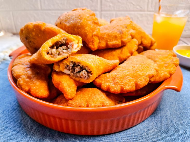 Pastéis prontos, servidos em mesa, com copo de suco ao fundo.