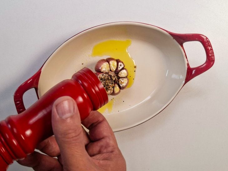 Alho sendo temperado com azeite, sal e pimenta antes de ir ao forno.