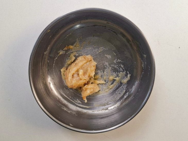Alho assado sendo amassado com um garfo até virar uma pasta cremosa.