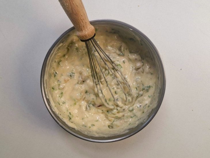 Ingredientes do patê sendo misturados em uma tigela com cheiro-verde e azeitonas picadas.
