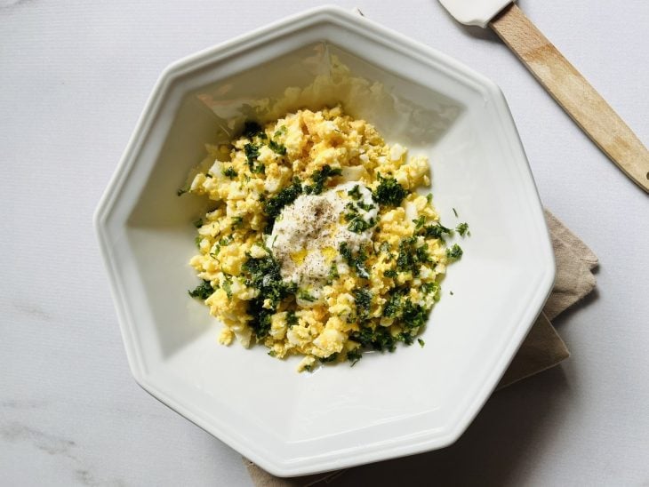 Ovos cozidos amassados, iogurte natural, azeite, sal, pimenta-do-reino e cheiro-verde misturados em uma tigela.