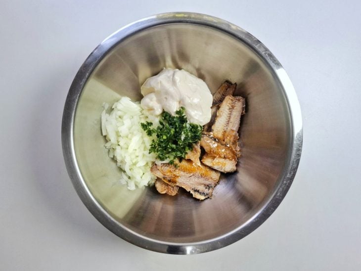 Sardinha, temperos e maionese adicionados em uma tigela de inox redonda.