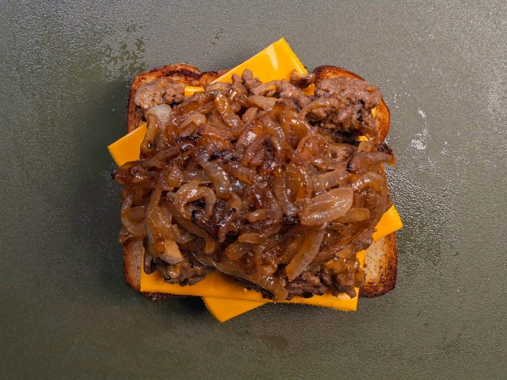 Fatia de pão com queijo, carne e cebola.