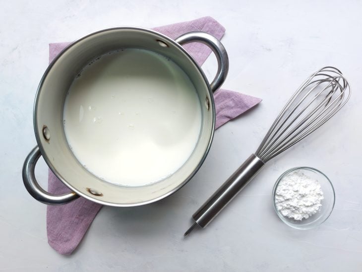 Panela com líquido branco e recipiente ao lado com ingrediente em pó branco.