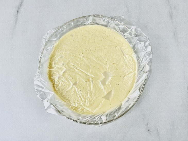 Creme branco em um recipiente de vidro coberto com plástico-filme.