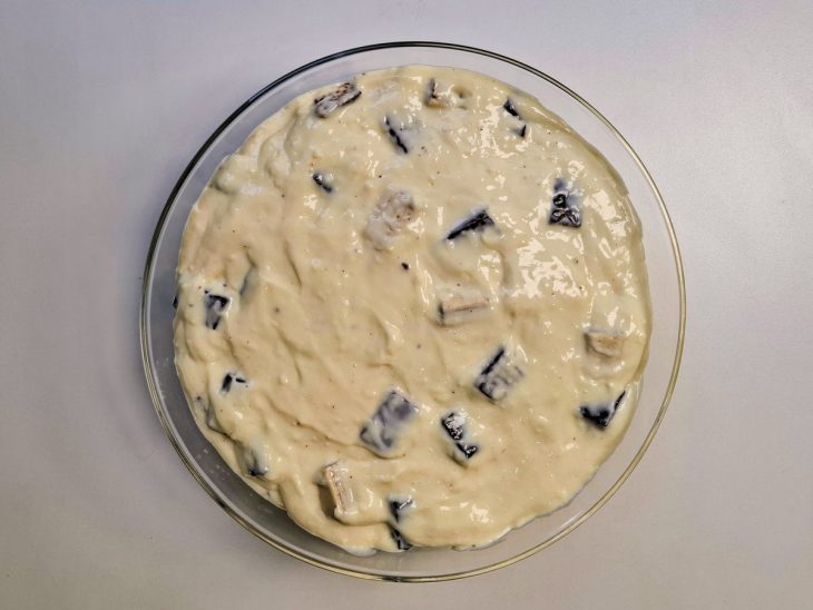 Pedaços de Bis colocados no creme branco acomodado na travessa.