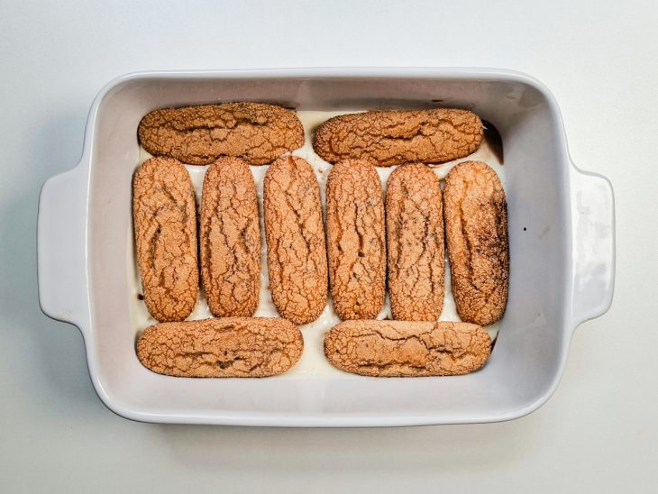 Camada de bolacha disposta sobre o creme branco no refratário.