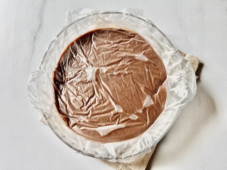Brigadeiro de chocolate preto em um prato de vidro coberto por um plástico.