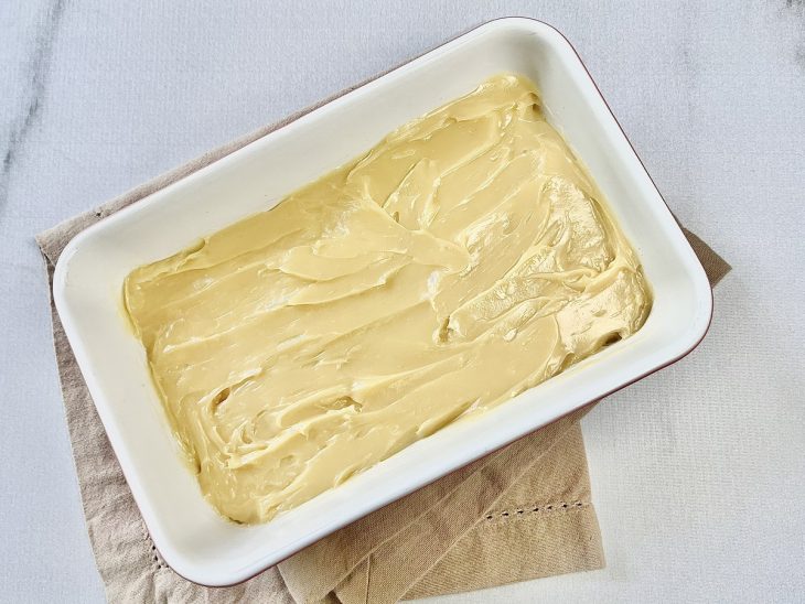 Creme de chocolate branco espalhado sobre os biscoitos dentro da travessa.
