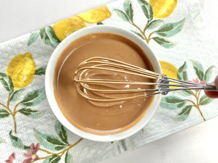 Um fouet e recipiente com creme de leite e chocolate derretido.
