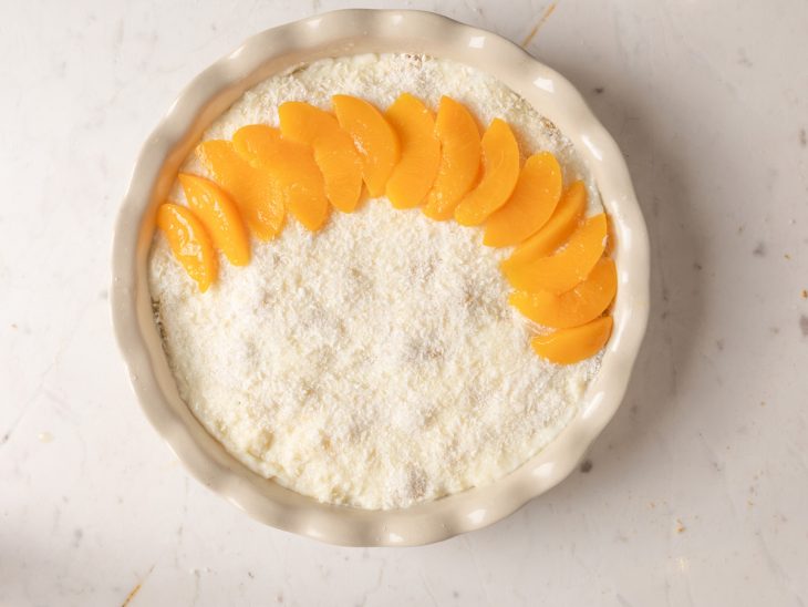 Camada de coco ralado e pêssegos sobrepostos no recipiente.