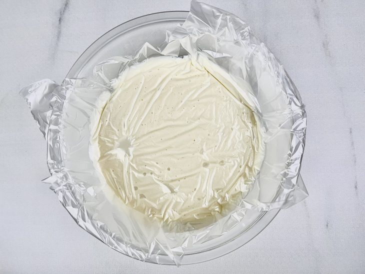 Creme transferido para uma tigela de vidro coberta com plástico.