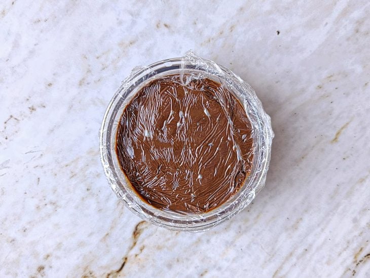 Creme de chocolate sendo transferido para travessa e coberto com plástico em contato.