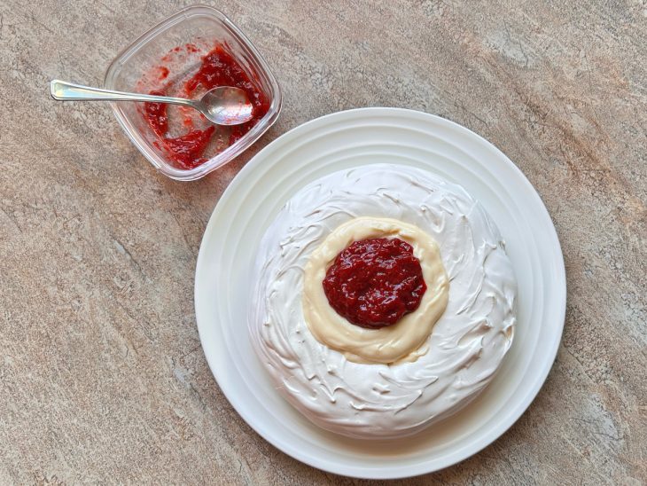 Em um prato de servir branco, a pavlova pronta, a tigela de geleia ao lado.