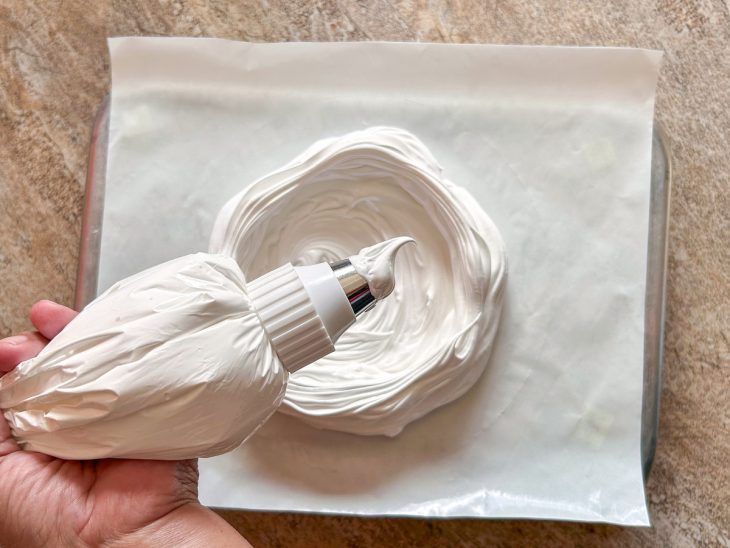 Numa superficie plana, há o papel antiaderente, e o merengue sendo moldado em cima.