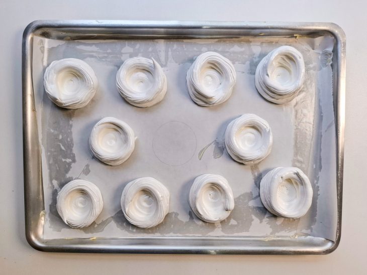 Merengue em formato de círculos em uma forma forrada com papel-manteiga.