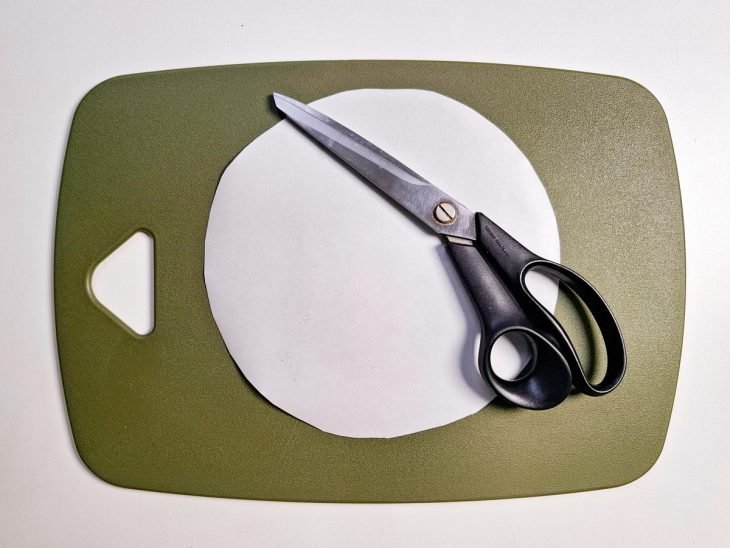 Disco de papel-manteiga cortado com auxílio de uma tesoura.
