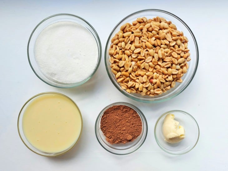 Ingredientes reunidos em diferentes recipientes: amendoim, açúcar, chocolate em pó, manteiga e leite condensado