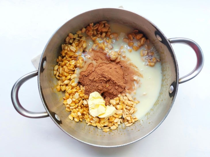Chocolate em pó, manteiga e leite condensado junto do amendoim e açúcar na panela de ferro.