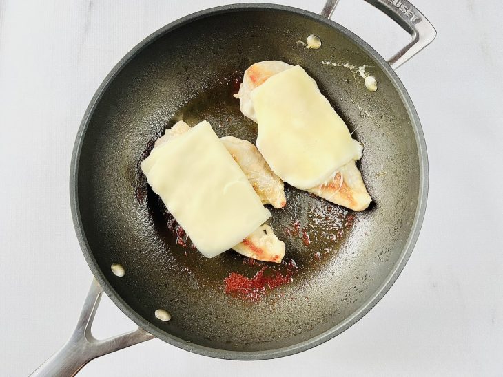 Os filés de frango na frigideiras, cobertos por fatias de muçarela.