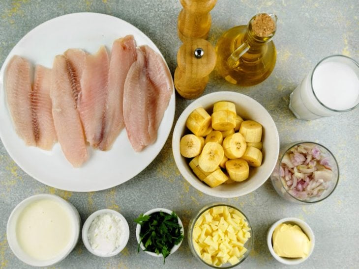 Ingredientes organizados na bancada com filés de tilápia, banana-da-terra e demais itens separados.